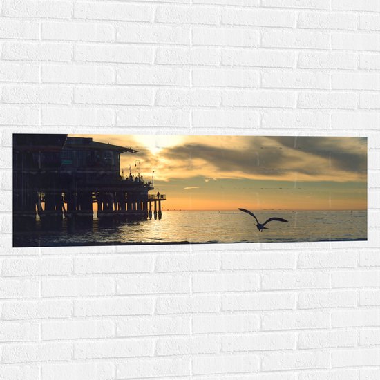Muursticker - Meeuw Vliegend Boven de Zee met aan de Zijkant een Leuk Strandtentje - 120x40 cm Foto op Muursticker