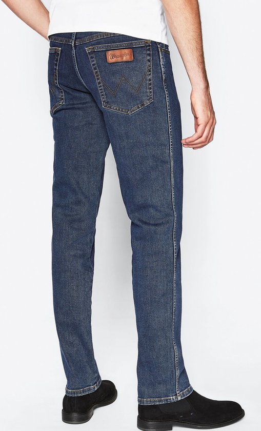 Man in spijkerblauwe Wrangler spijkerbroek, gezien vanaf de achterkant rechts.