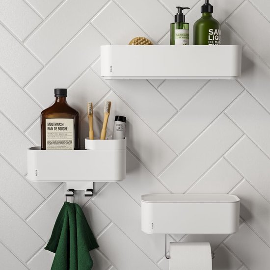Trois solutions de rangement Tiger blanches sur un mur carrelé blanc à motif chevrons. Deux avec compartiment ouvert, un avec porte-rouleau.