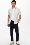 Man met een beige linnen mix overhemd met korte mouwen, een witte t-shirt en een zwarte broek.