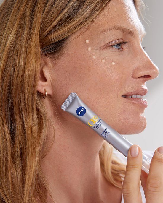 Vrouw met blond haar past NIVEA Q10 Anti-Rimpel Expert serum toe, met kleine productdruppels op haar gezicht.