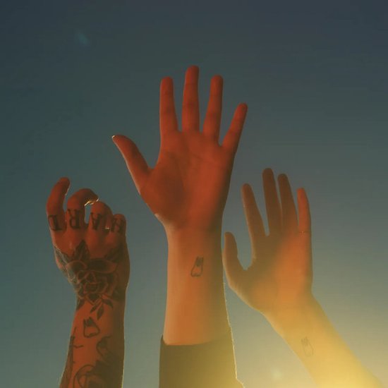 Trois mains, dont une tatouée, levées vers un ciel bleu avec un soleil couchant.