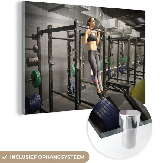 MuchoWow® Glasschilderij - Een blanke vrouw doet pull ups in een fitness gym - 120x80 cm - Acrylglas Schilderijen - Foto op Glas