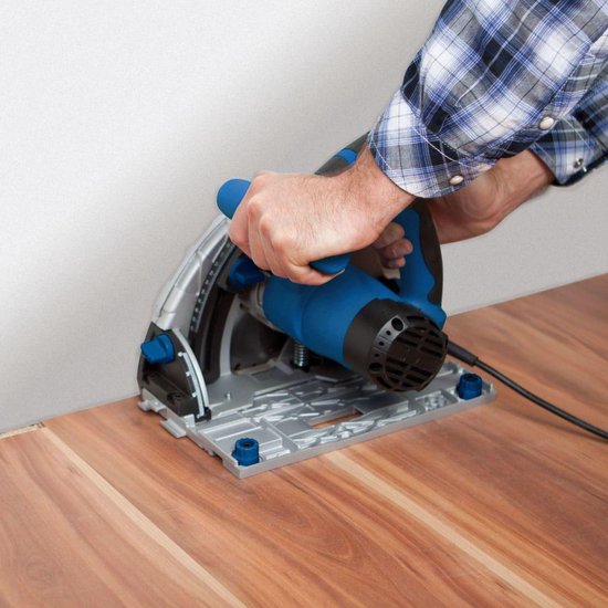 Persoon met blauwe en zilverkleurige invalzaag zaagt in een houten vloer. Gemonteerd op een zilverkleurige voet.