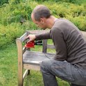 Man schuurt een houten bankje in de tuin met een rode Einhell multischuurmachine.