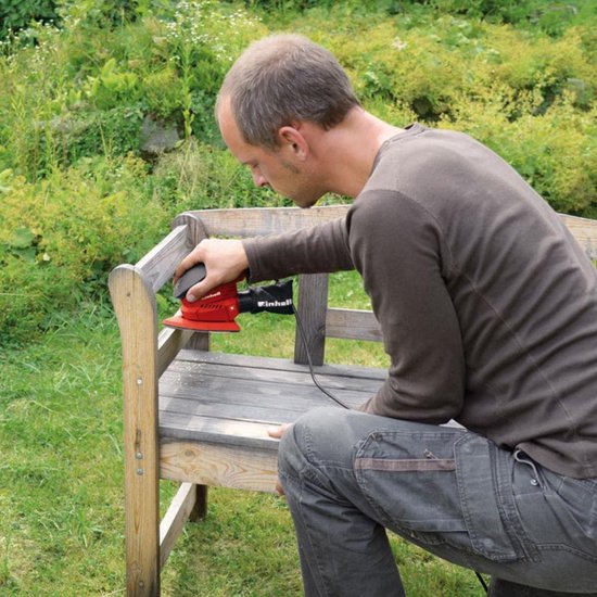 Man schuurt een houten bankje in de tuin met een rode Einhell multischuurmachine.
