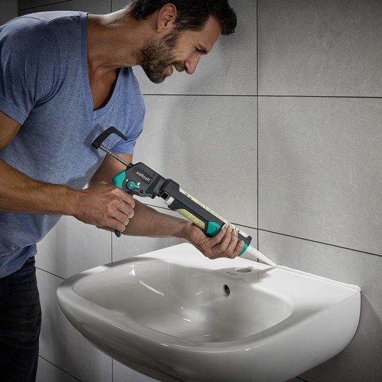 Man in blauw shirt gebruikt een wolfcraft kitpistool met groene en zwarte accenten om een wastafel af te kitten.