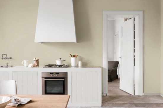 Lichte groene muur in een keuken met aanrecht, oven en open deur naar een andere kamer.