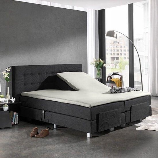 Verstelbaar bed met creme splittopper hoeslaken, donkergrijs gestoffeerd hoofdbord en ombouw.