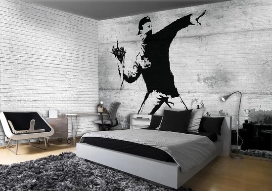 Muurschildering met een man in zwart-wit die bloemen gooit, tegen een bakstenen muur.