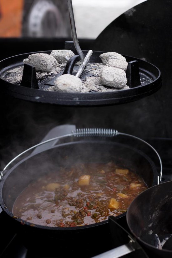 Gietijzeren Dutch oven met stoofpot, onder een deksel met kolen op het deksel.