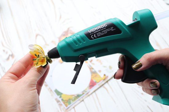 Hand wordt gebruikt om een kleine gele bloem te bevestigen aan het groene VONROC lijmpistool.