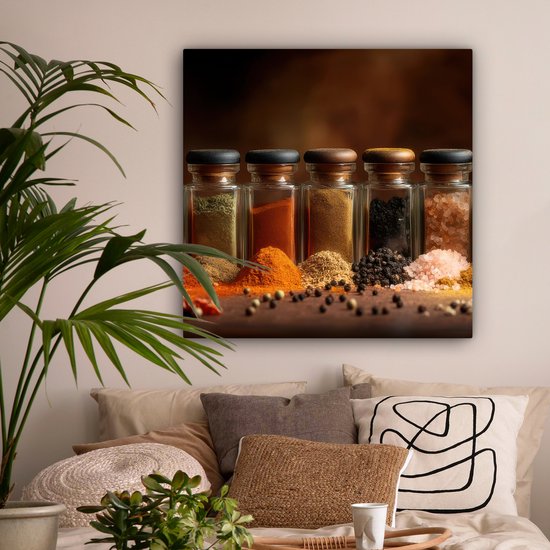 Vijf glazen potjes gevuld met specerijen: groen, rood, bruin, zwart en roze zout. Met hoopjes kruiden voor de potjes.