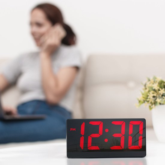 Digitale wekker met rood display dat 12:30 weergeeft, op een tafel.