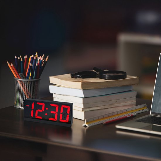 Digitale wekker met rood display dat 12:30 weergeeft, op een bureau met boeken.