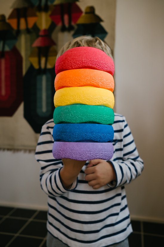 Een kind met een gestreept shirt houdt een stapel van zeven regenboogkleurige Stapelstein® Classic mini stapelspeeltjes vast.