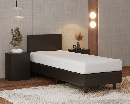 Zwarte boxspring met wit matras, naast een nachtkastje met plant.