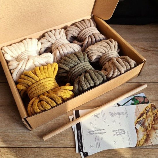 Kartonnen doos met 8 strengen Bobbiny Jumbo garen in diverse aardetinten, inclusief instructies en een houten stok.