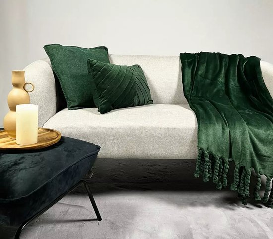 Donkergroene fleece plaid met franjes op een lichte bank, naast groene kussens.