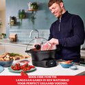 Man bereidt sous-vide voedsel in een zwarte multicooker met een digitale timer. Ingrediënten zoals rundvlees, tomaten en champignons.