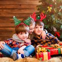 Trois enfants avec des serre-têtes de Noël, un arbre de Noël, des bois de renne, une tête de Père Noël.