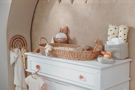 Witte commode met rotan aankleedmand vol baby spulletjes, decoraties en speelgoed.