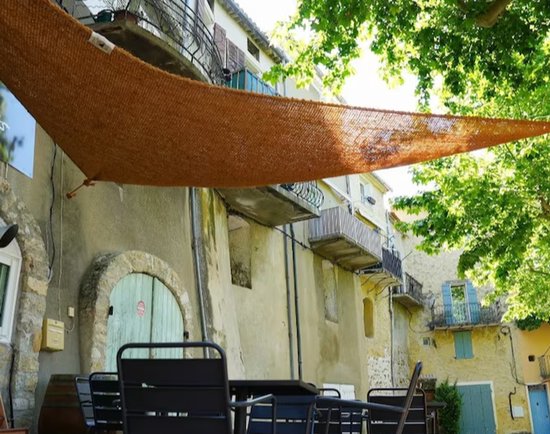 Een bruin kokosvezel schaduwdoek hangt over een terras met tafels en stoelen.