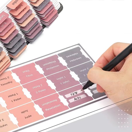 Hand die bijbel tabsticker 'Acts' opplakt, met stickers met titels zoals 'Titus', 'Philemon', 'Hebrews'.