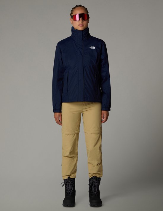 Dames in donkerblauwe The North Face jas, beige broek, zonnebril en zwarte laarzen.