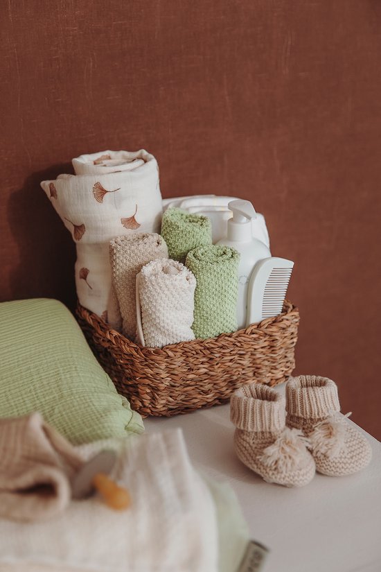 Mand gevuld met opgerolde witte en groene luiers, babydoekjes en een flesje.