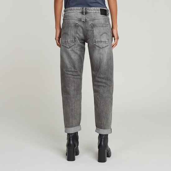 Model draagt een grijze jeans met opgerolde broekspijpen en zwarte laarzen.