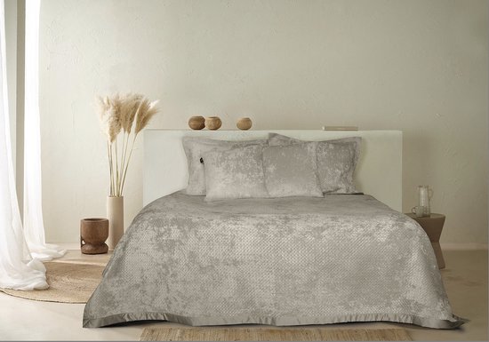 Een slaapkamer met een bed opgemaakt met een taupekleurige sprei, kussens en decoratie.