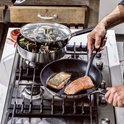 Man bakt zalm in koekenpan. Mosselen in een pan met deksel ernaast.