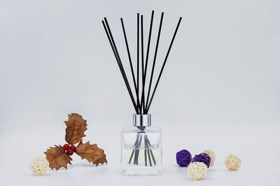 Glazen diffuserfles met een zilveren dop, gevuld met heldere vloeistof en zwarte stokjes, omringd door decoratieve kerstversieringen.