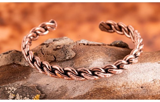 Koperen armband met een gedetailleerd gevlochten patroon, rustend op een stuk hout.