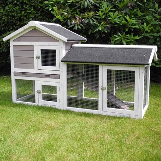 Konijnenhok met wit frame, grijs houten huisje met twee verdiepingen, gaasdeuren en een ren. Het hok staat op een grasveld.