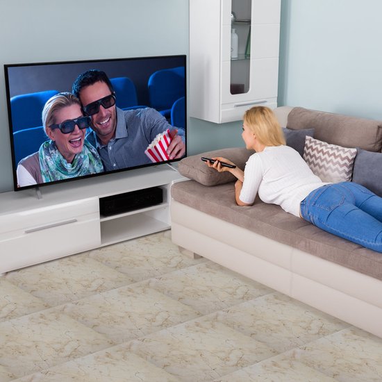 Vrouw met afstandsbediening kijkt naar 3D-film op tv met popcornaan. Op de bank liggen kussens.