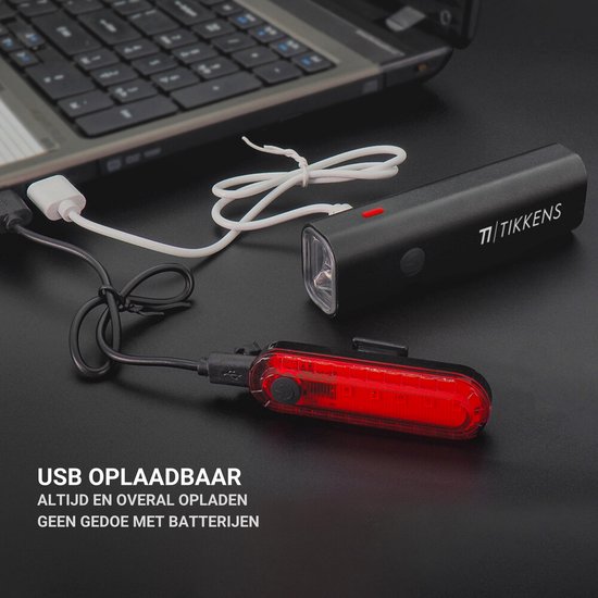 Lampe de vélo noire Tikkens et feu arrière rouge, connectés via des câbles USB à un ordinateur portable pour le chargement.