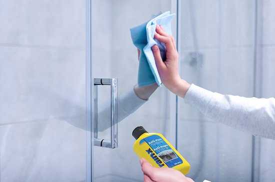 Hand die een glazen douchedeur schoonmaakt met een blauwe doek, naast een fles Rain-X.