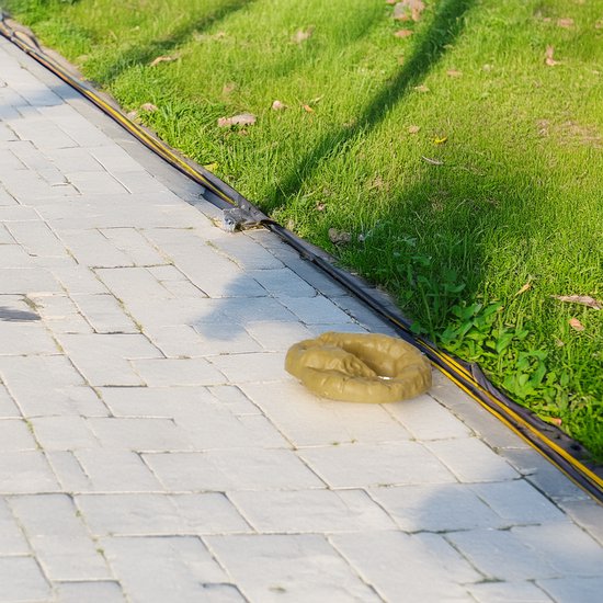 Een realistische kunsthondendrol op een betegeld looppad naast gras.