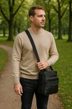 Man met beige trui en zwarte jeans draagt een zwarte leren schoudertas.