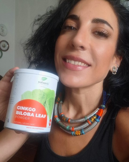 Vrouw met een ketting en oorbellen, die een blik Nature's Finest Ginkgo Biloba poeder vasthoudt.