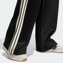 Voeten in zwarte trainingsbroek met wijde pijpen en beige 3-strepen, met sneakers.