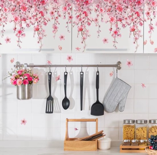 Roze bloesemtakken boven keukenkastjes met keukengerei en potten, op een betegelde muur met losse bloesems.