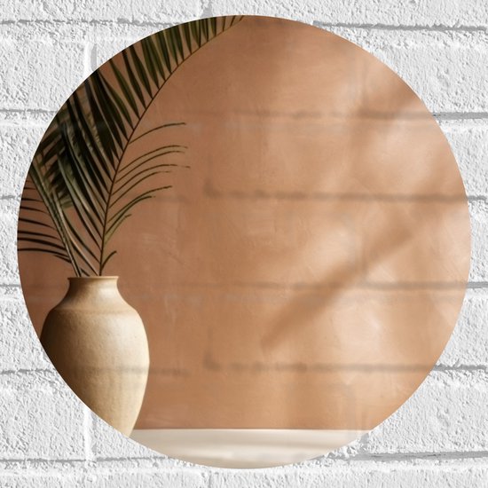 Close-up van een bruine keramieken vaas met groene palmbladeren, tegen een natuurkleurige muur met schaduwen.