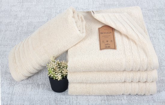 Stapel van drie beige Betully handdoeken met een opgerolde handdoek en plantje.