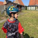 Jongen met groene dinosaurushelm en rood-zwart shirt in de tuin.