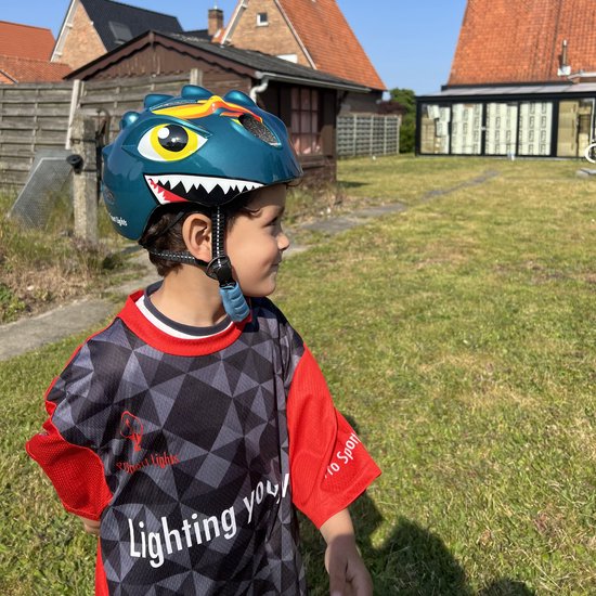 Jongen met groene dinosaurushelm en rood-zwart shirt in de tuin.