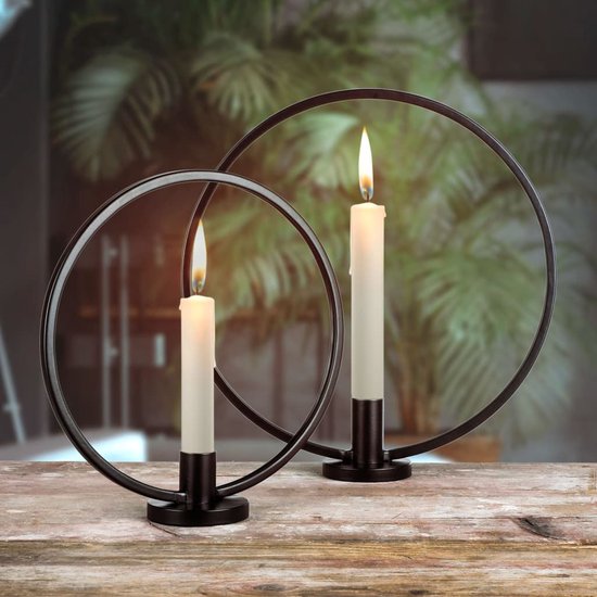 Twee zwarte ringkandelaren met witte kaarsen, op een houten tafel.