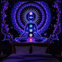 Een slaapkamer met een wandkleed van een yogi in meditatie, met mandala, boven een bed. De verlichting is paars.